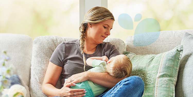 A woman holding her sleepy baby while sitting on the couch during the daytime.